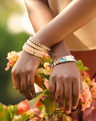 Close-up of hands wearing multiple bracelets on a floral background