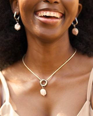 Woman wearing a gold necklace with a pendant, close-up of neck and earrings.