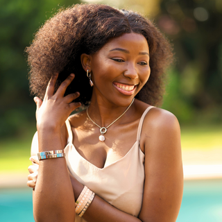 Woman with curly hair smiling outdoors with a blurred natural background