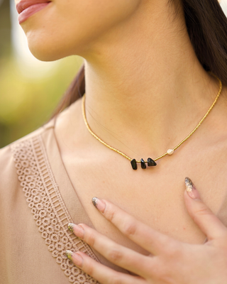 Gold necklace with black stones worn by a person outdoors