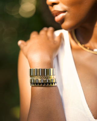 Woman wearing gold bracelets on a blurred natural background