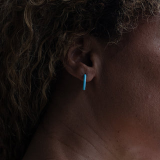 A woman wearing turquoise hoop earrings that add a fresh pop of colour to an effortlessly modern look.