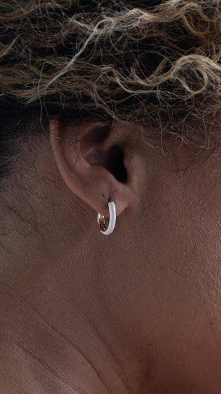A close-up of a woman wearing white resin hoop earrings with gold detailing, bringing a fresh, minimalist touch to an elegant look.