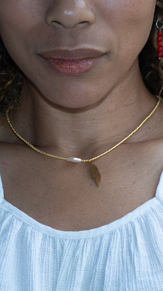 A lady wearing a gold necklace with a feather pendant and freshwater pearl, creating a graceful finishing touch for effortless everyday style.