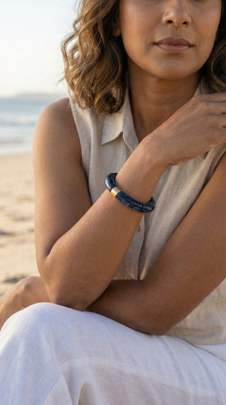 A woman relaxing by the beach wearing a deep navy resin bracelet, effortlessly pairing bold colour with a light, elegant summer look.