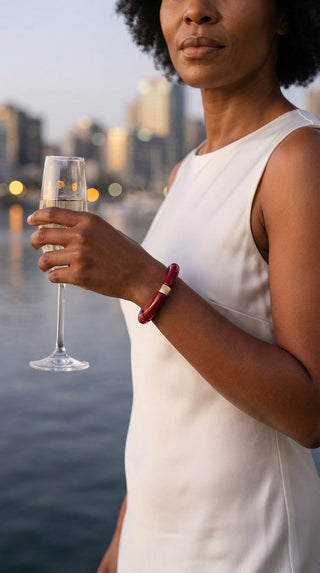 A fashionable lady wearing a deep burgundy resin bracelet while enjoying an evening by the water, adding a sophisticated statement to a refined, effortless look.