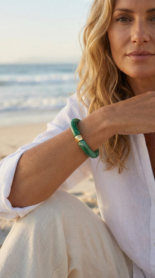 A stylish woman wearing a marbled green resin bracelet by the seaside, effortlessly pairing its earthy tones with a fresh, relaxed wardrobe.