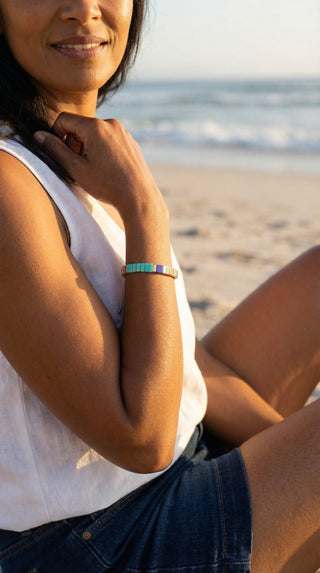 A woman wearing a colourful turquoise beaded bracelet with coral, blue, pink, and gold accents, adding a playful yet elegant touch to a relaxed summer outfit.