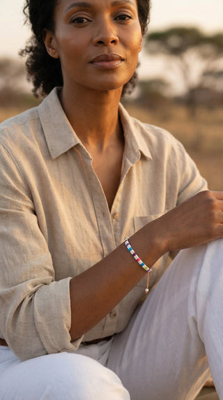 A woman wearing a colourful white tile beaded bracelet with vibrant rainbow accents, adding a playful pop of colour to a relaxed linen outfit for effortless everyday style.
