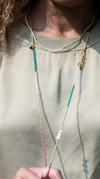 A woman wearing a colourful layered beaded necklace with turquoise, aqua, coral, white, and gold accents, creating a relaxed coastal-inspired look that adds effortless elegance to everyday style.