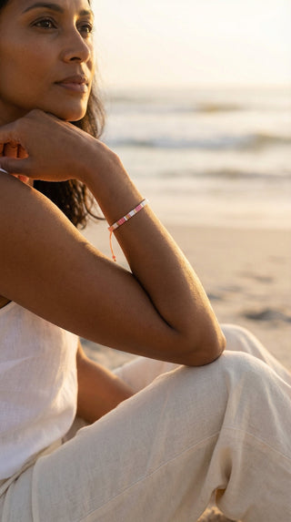 A woman wearing a pink and white Miyuki tile beaded bracelet with gold accents, adding a subtle touch of colour and effortless elegance to a relaxed beach-inspired look.