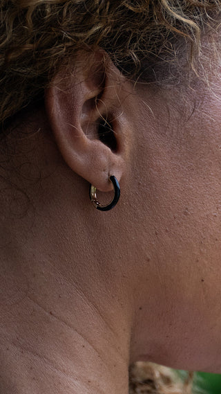 A close-up captures elegant black resin hoops framing the ear, blending contemporary design with everyday sophistication.